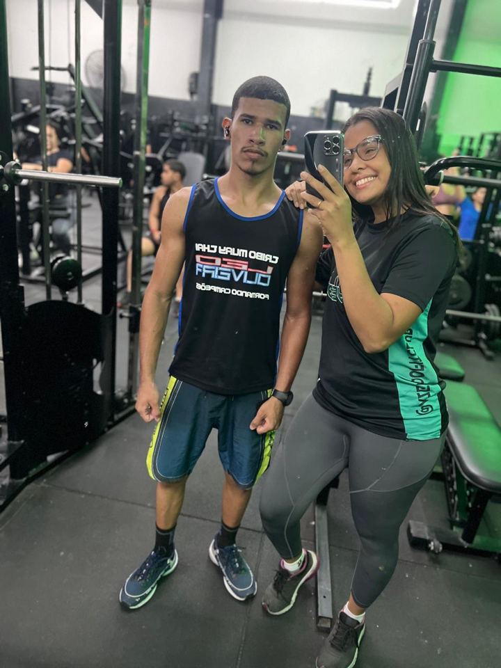 Lis ao lado de um aluno na área de musculação